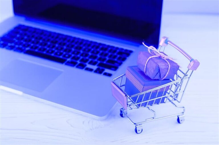 Carrinho de compras em miniatura com pacotes em frente a um notebook, representando vendas online com automação no e-commerce via WhatsApp.