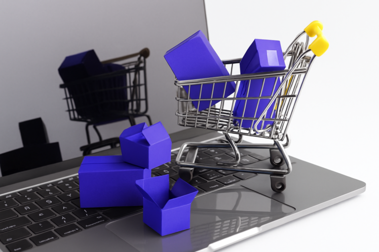 Carrinho de compras com caixas roxas em cima de um notebook, simbolizando vendas online.